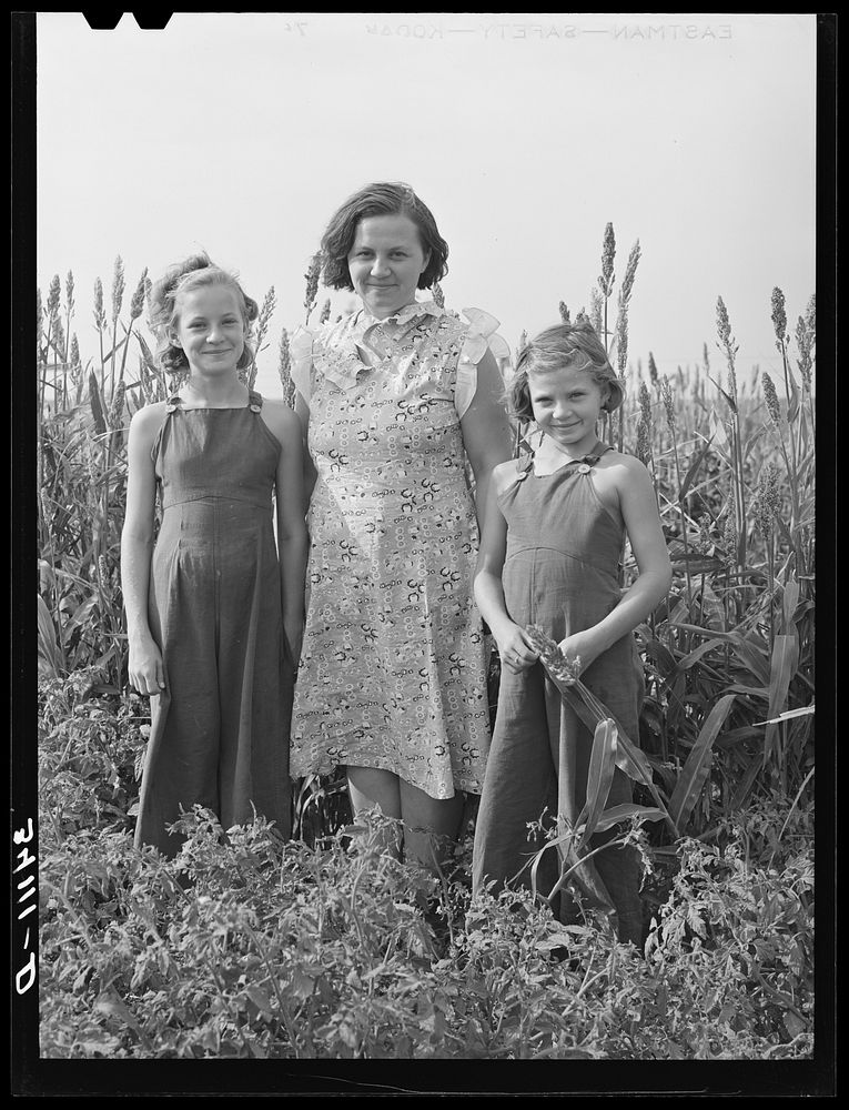 Wife of FSA (Farm Security Administration) client with her two daughters in garden. Kaffir corn in background is used as…
