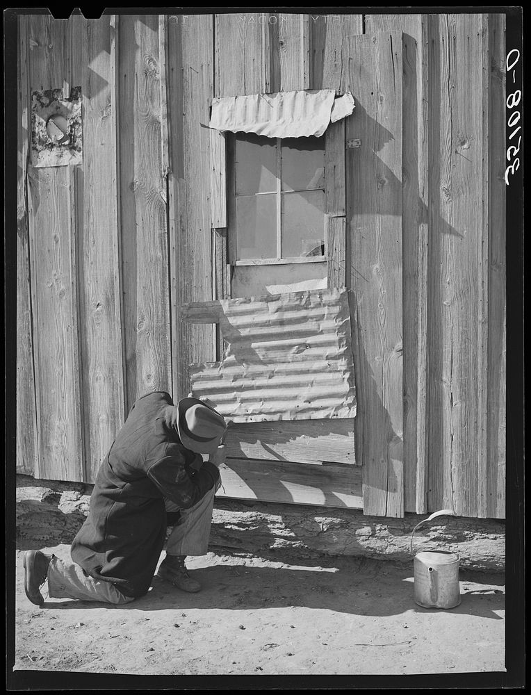 Pomp Hall,  tenant farmer, repairing piece of tin which covers window of his house. Creek County, Oklahoma by Russell Lee