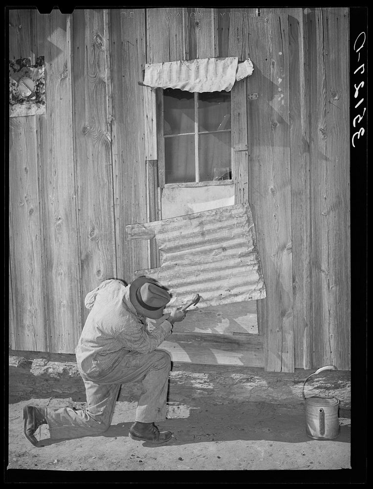 Pomp Hall,  tenant farmer, repairing piece of tin which covers window of his house. Creek County, Oklahoma. See general…