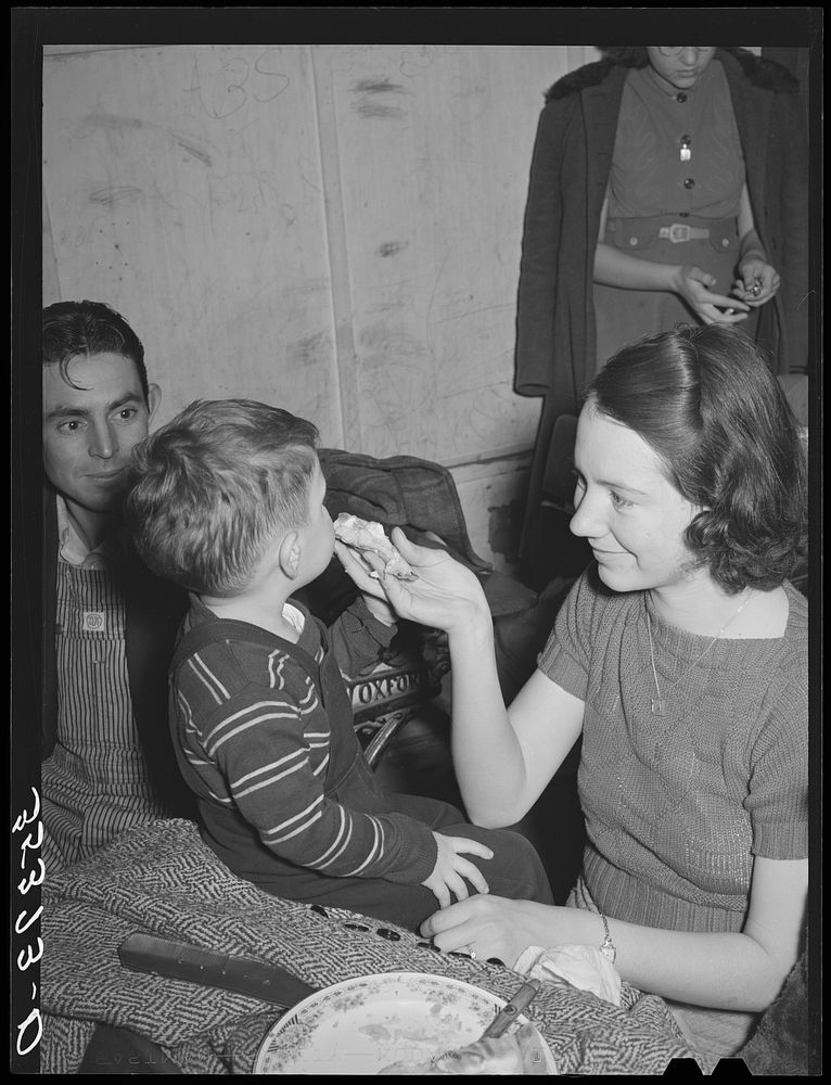 Farm mother feeding pie to her son while the father watches. Pie supper in Muskogee County, Oklahoma. See general caption…