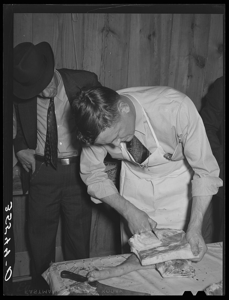 FSA (Farm Security Administration) supervisor slicing bacon during meat cutting demonstration before FSA officials and…