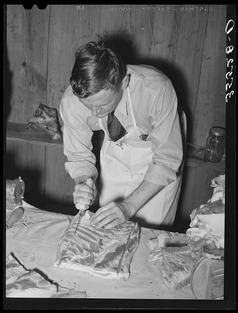 FSA (Farm Security Administration) supervisor giving a demonstration of meat cutting before a group of FSA officials and…