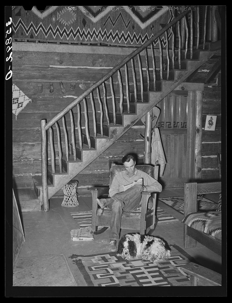 Manager of the Navajo Lodge with his dog before the fireplace on a snowy afternoon. Datil, New Mexico by Russell Lee