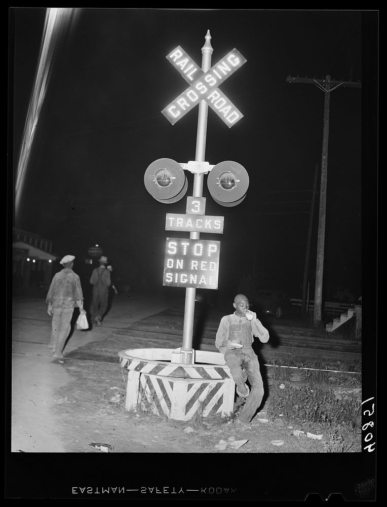 Migratory agricultural worker has his supper (a nickle pie and a glass of milk) at the railroad crossing at Camden, North…