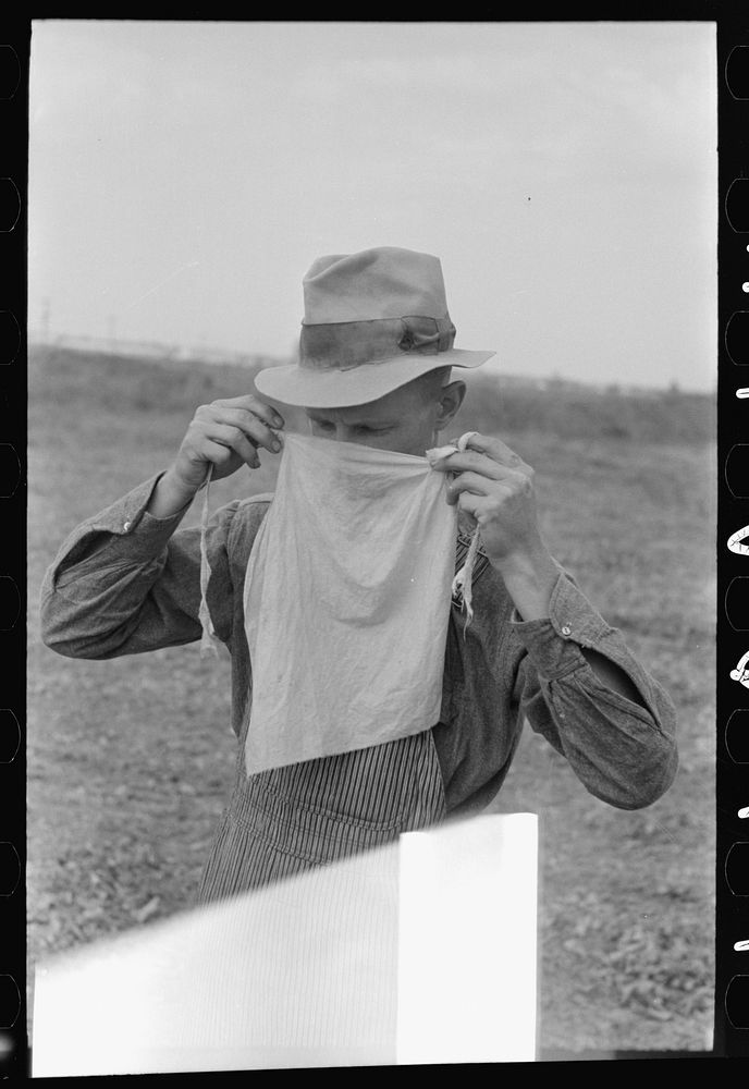 Farmer adjusting mask to avoid dust in haying operations. Lake Dick Project, Arkansas by Russell Lee