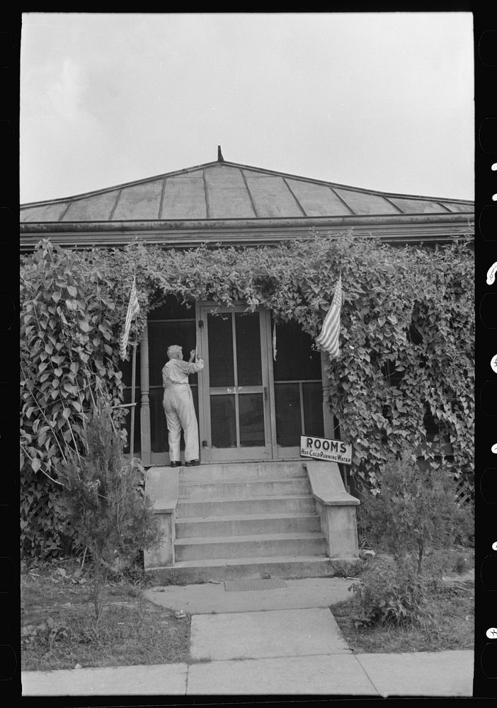 [Untitled photo, possibly related to: Man taking up flag in front of house to provide local atmosphere for state fair…