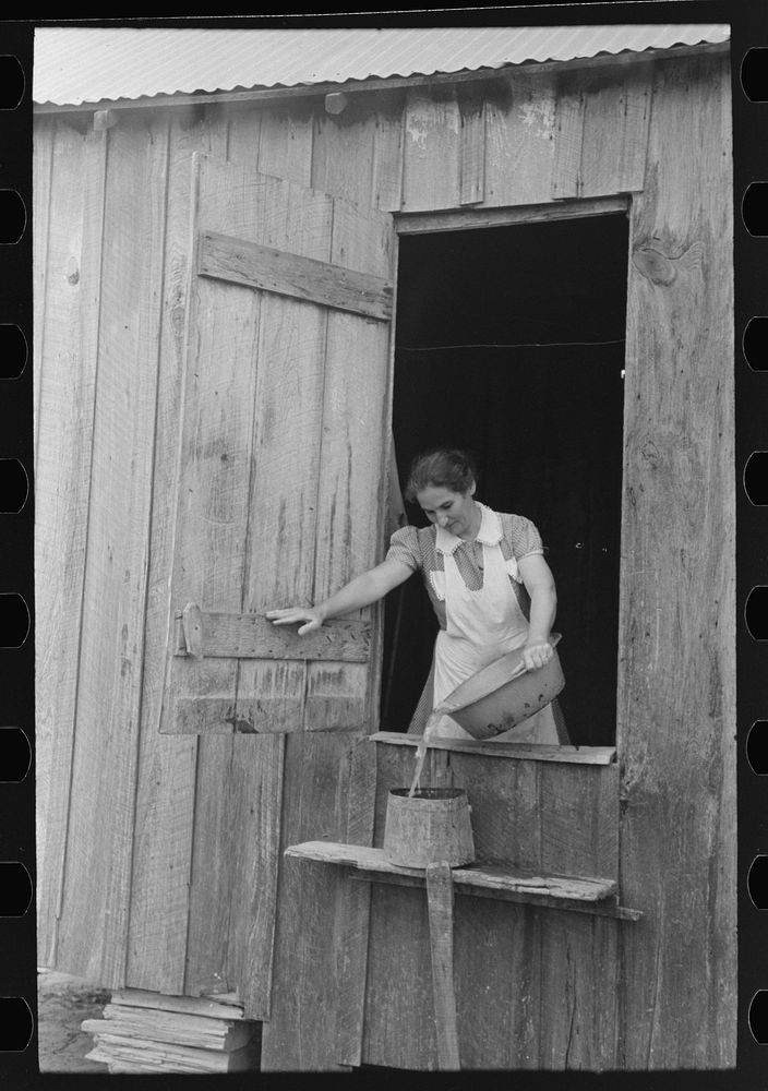 Wife of FSA (Farm Security Administration) client who will participate in the tenant purchase pouring dishwater into slop…