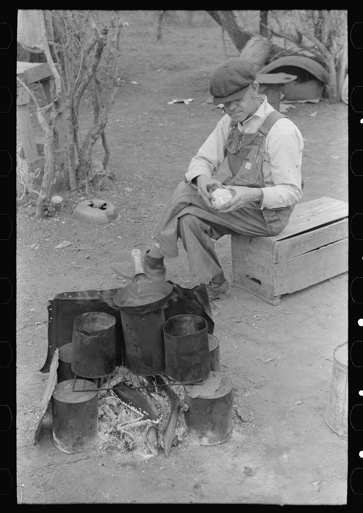 [Untitled photo, possibly related to: White migrant worker sawing wood for stakes to be used in setting up tent home, near…