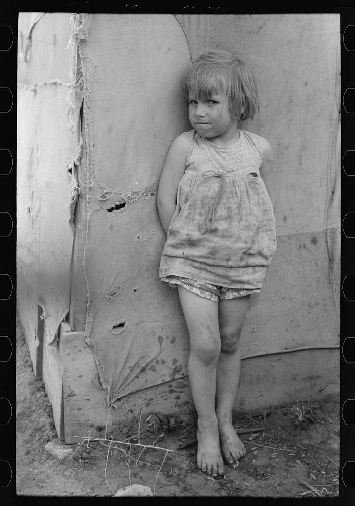 Child of white migrant worker standing by tent home near Harlingen, Texas by Russell Lee