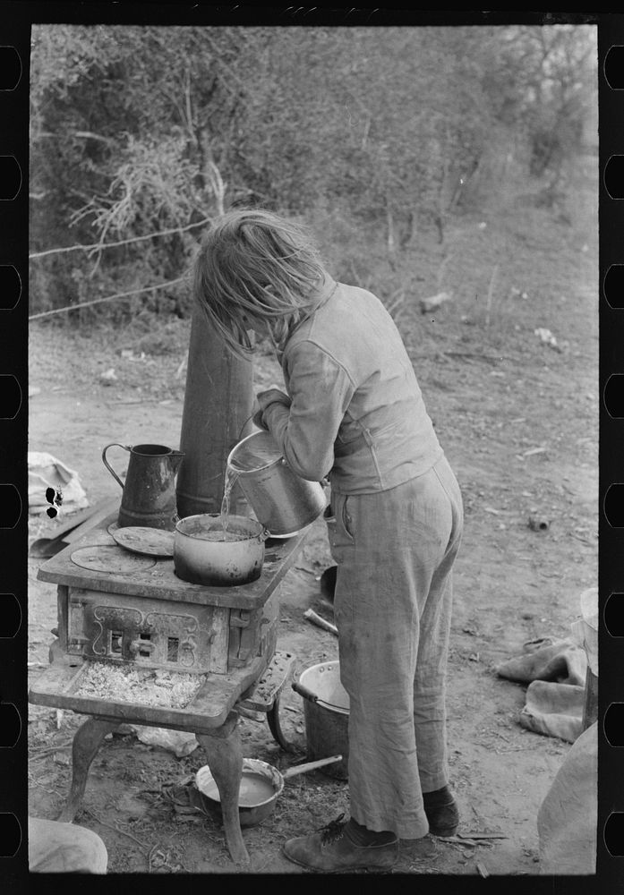 Child of white migrant adding water to boiling beans on stove which was set up immediately after reaching camping grounds…