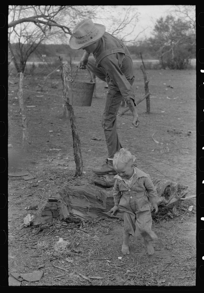 Child of white migrant climbing fence with pail of water near Harlingen, Texas by Russell Lee