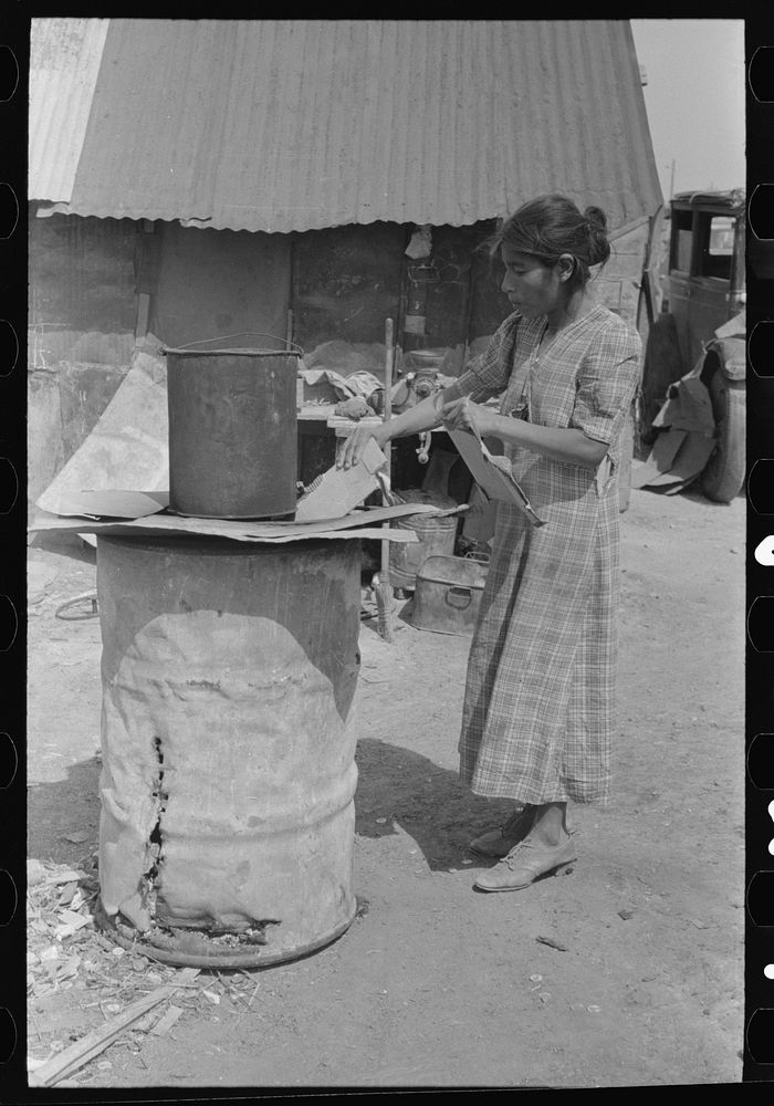 Mexican woman building fire in battered steel drum in backyard of her house, San Antonio, Texas by Russell Lee