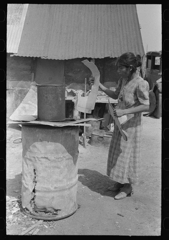 [Untitled photo, possibly related to: Mexican woman building fire in battered steel drum in backyard of her house, San…