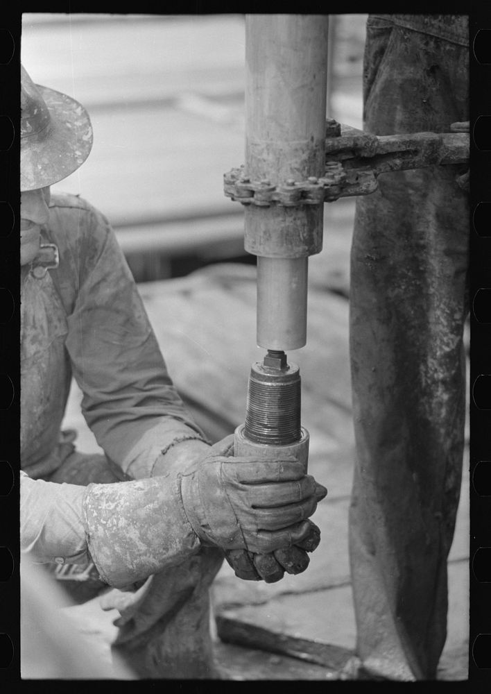 Oil field worker screwing on a nipple, Kilgore, Texas by Russell Lee