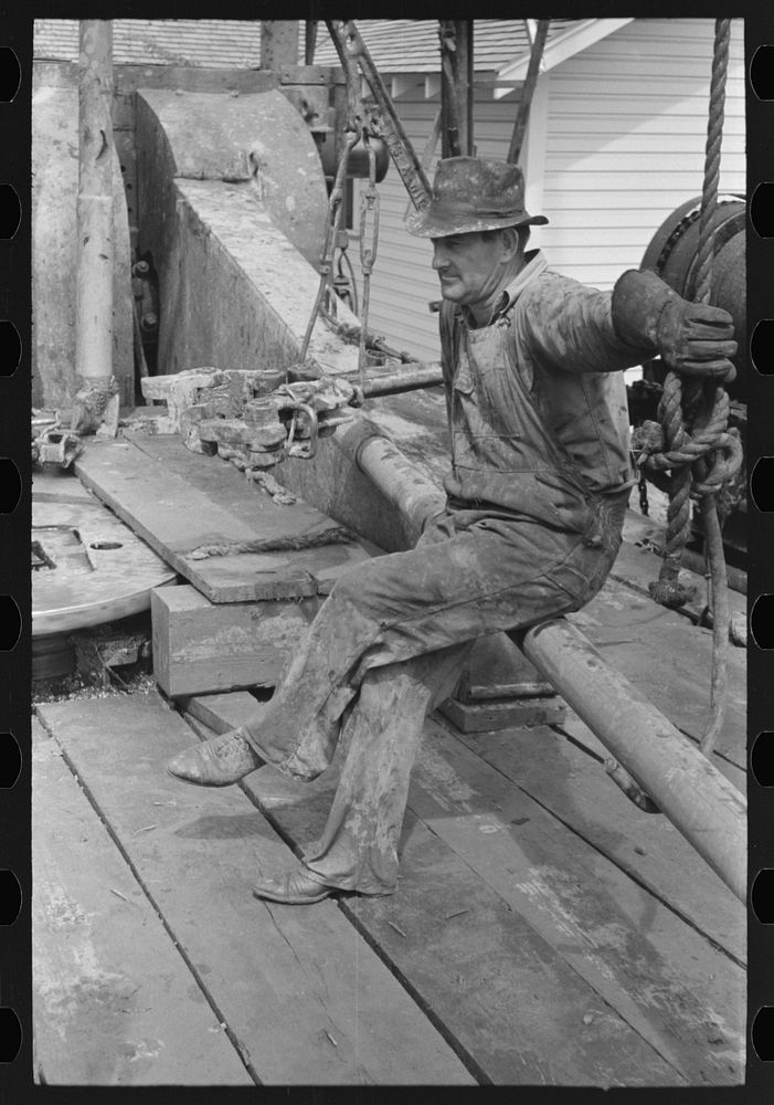 Oil field worker resting on a length of pipe, Kilgore, Texas by Russell Lee