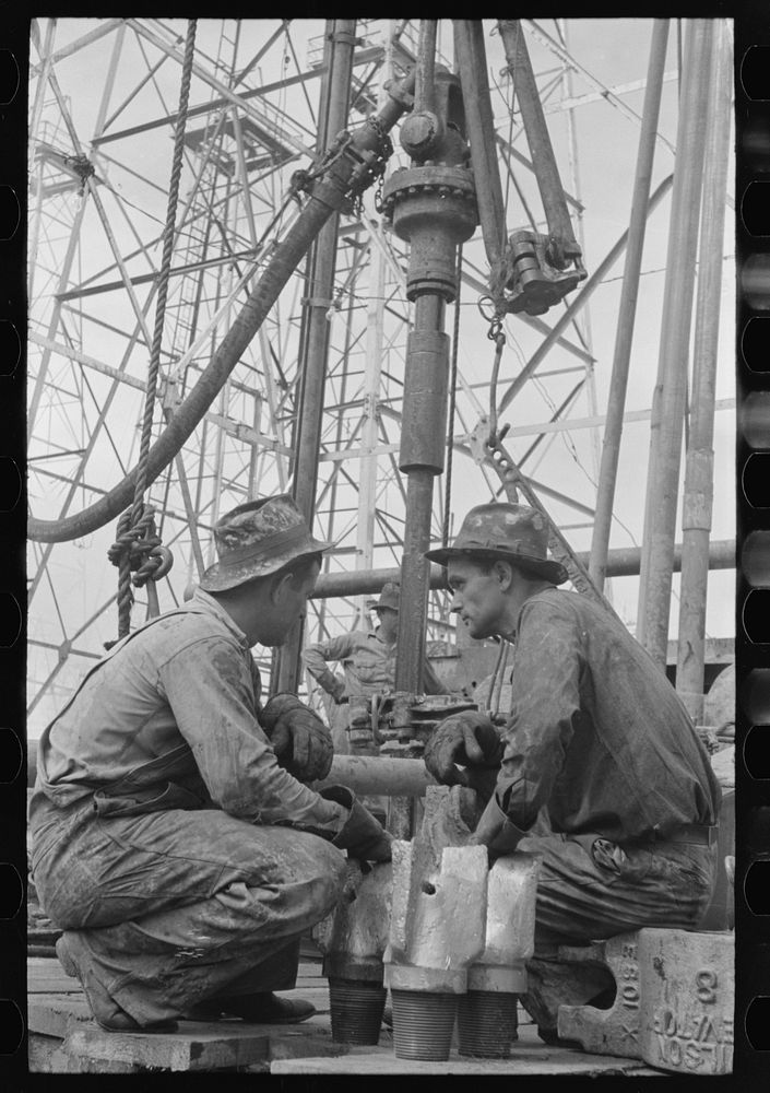 [Untitled photo, possibly related to: Oil drillers talking with bits in front of them and drilling equipment in background…