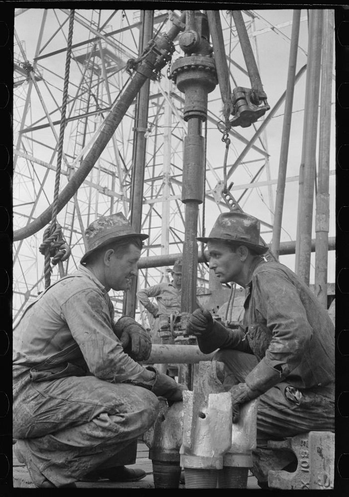 Oil drillers talking with bits in front of them and drilling equipment in background, Kilgore, Texas by Russell Lee
