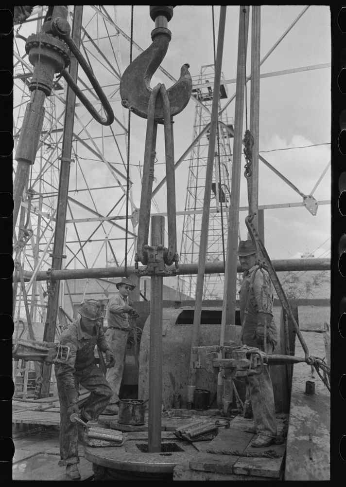 [Untitled photo, possibly related to: Oil field workers, reaching for clamp on elevator. The elevator removes the pipe from…