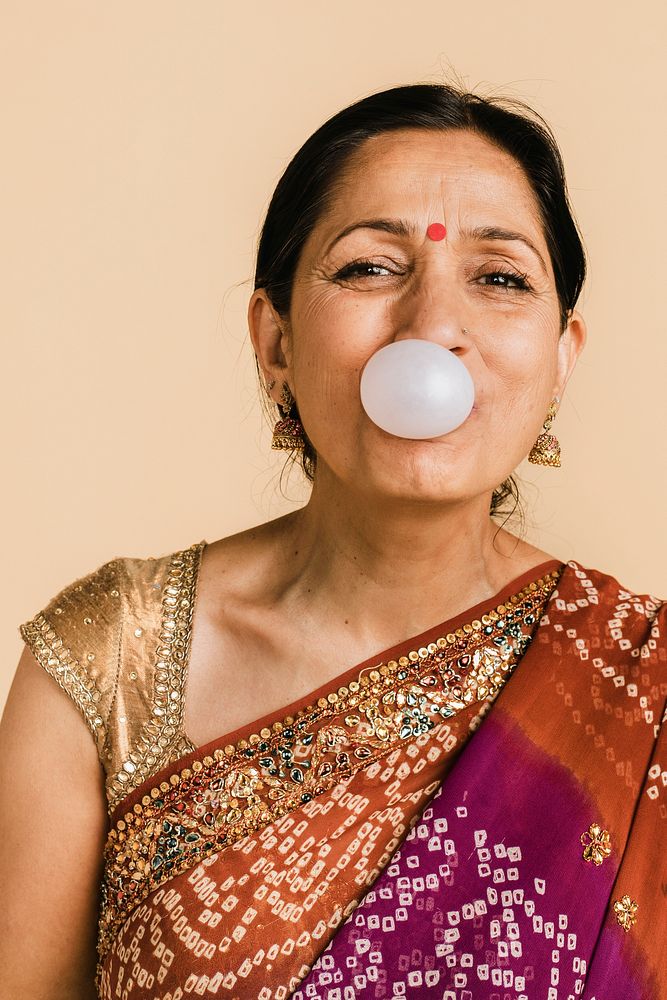 Senior Indian woman in a traditional saree blowing a bubble with a chewing gum 