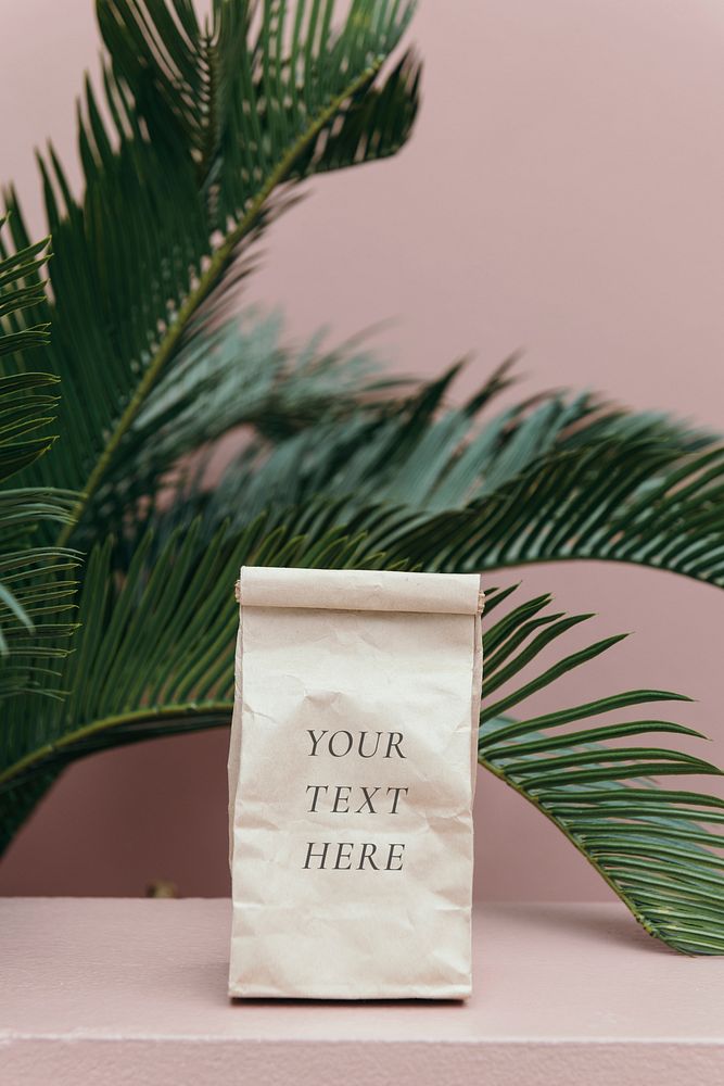 Paper bag mockup in a pastel pink room by a palm tree