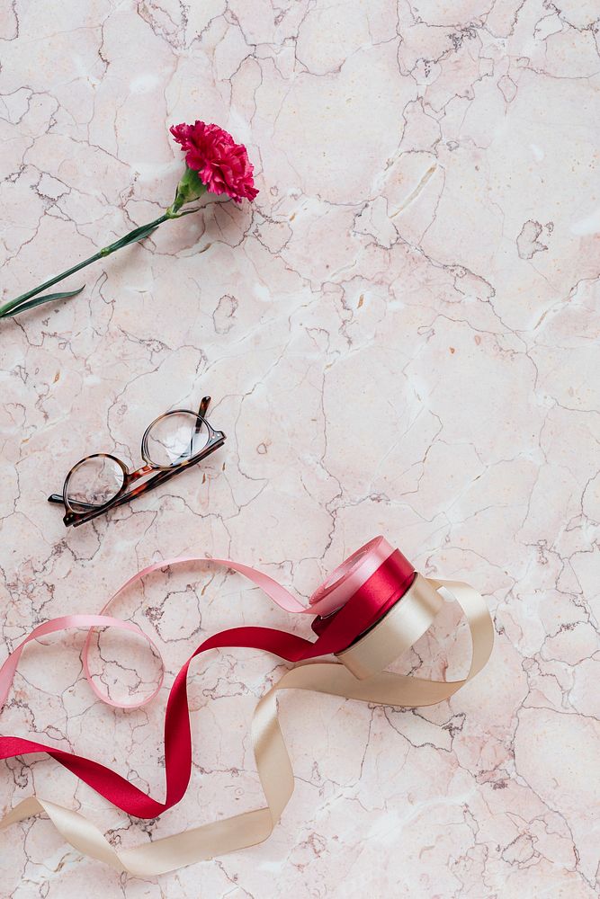 Red carnation and ribbons on a pink marble background