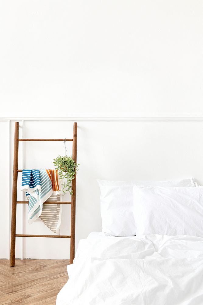 Wooden ladder clothes rack by a white bed