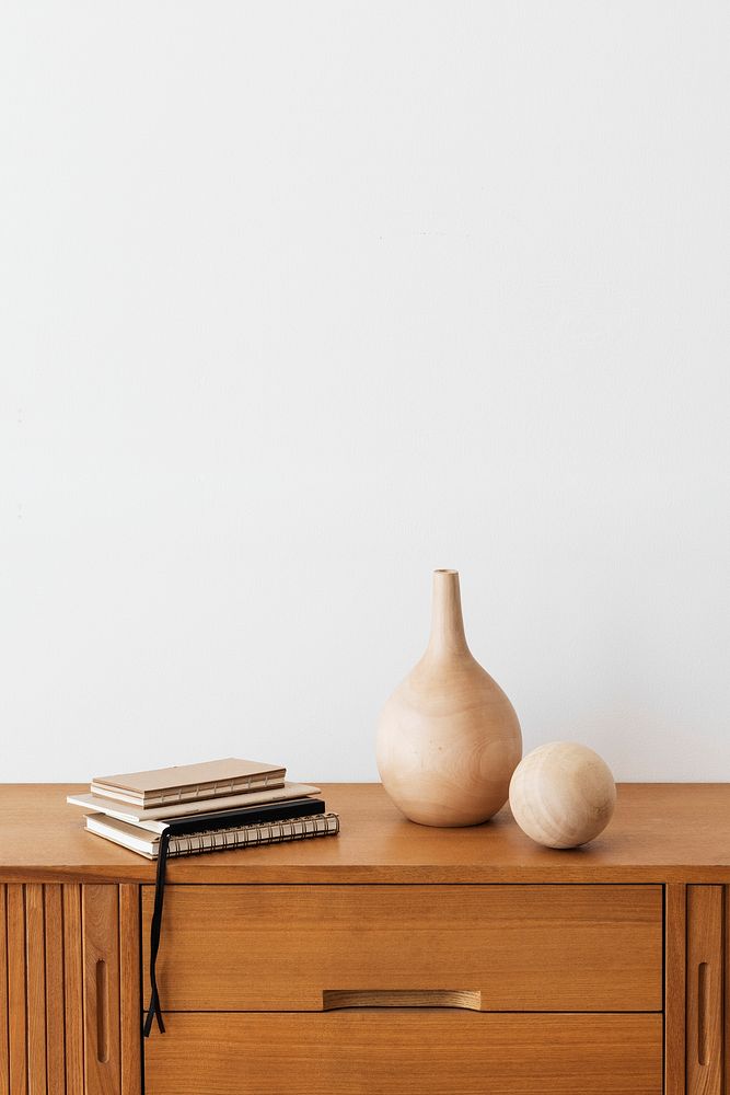 Stack of notebooks by a wooden vase on a wooden cabinet in a white room
