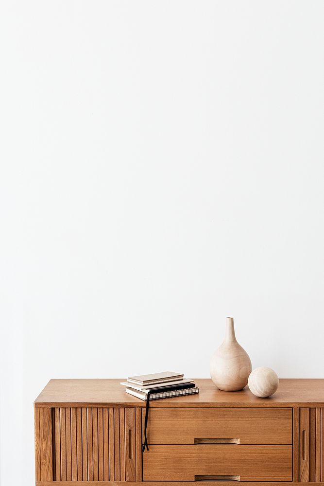 Stack of notebooks by a wooden vase on a wooden cabinet in a white room