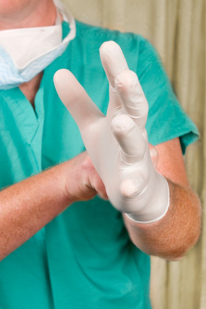 A healthcare provider donning a pair of green latex gloves in order to protect herself during her subsequent interaction her…