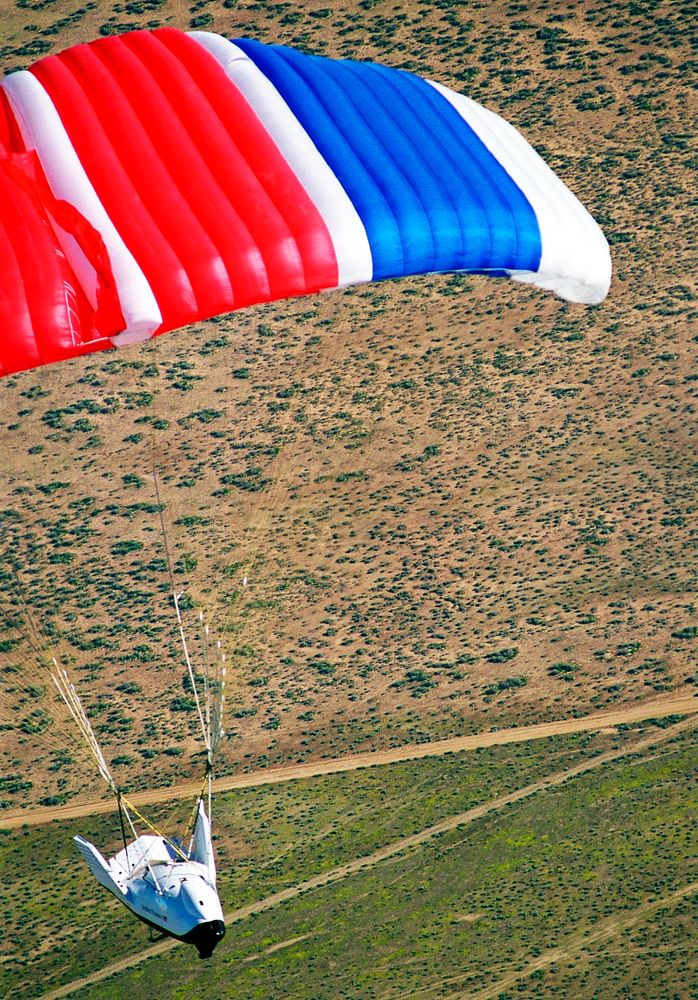 The X-38 Crew Return Vehicle descends under its steerable parafoil over the California desert in its first free flight at…