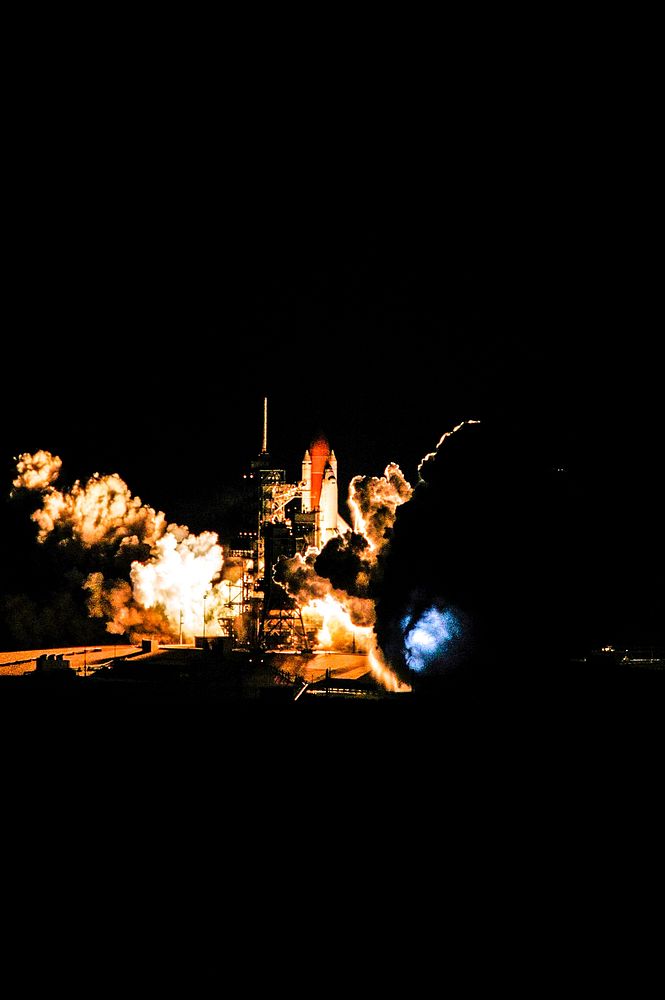At liftoff from Launch Pad 39B, Space Shuttle Discovery spreads a blaze of light as it leaps into the night sky over Kennedy…