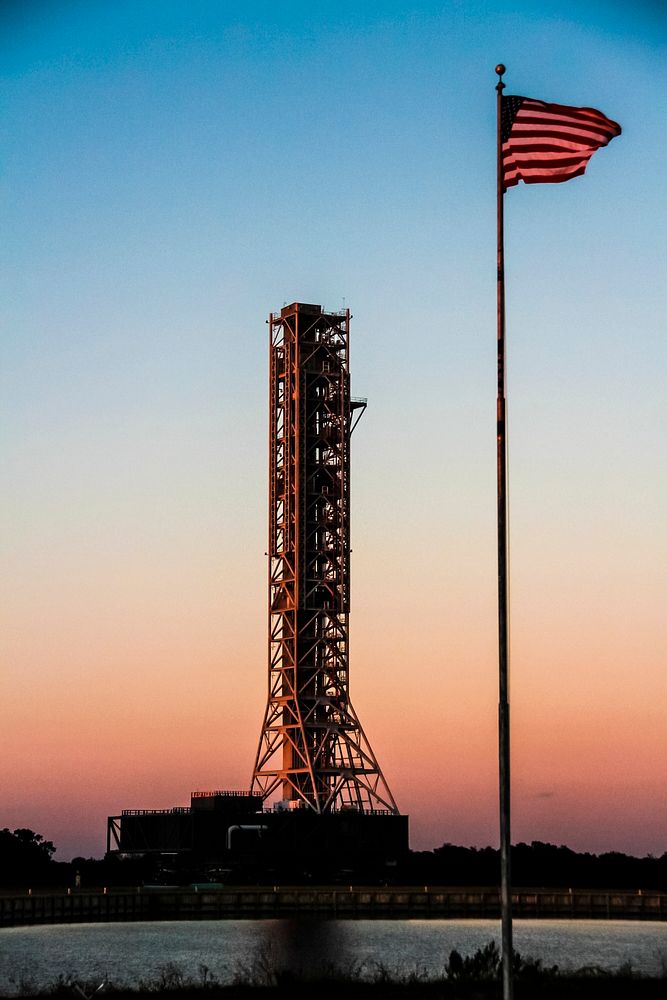 The flag at NASA's Press Site is on guard as the mobile launcher, or ML, passes by the turn basin at NASA's Kennedy Space…