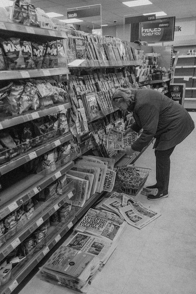 Woman reading coronavirus news from a newspaper at the supermarket. BRISTOL, UK, March 30, 2020