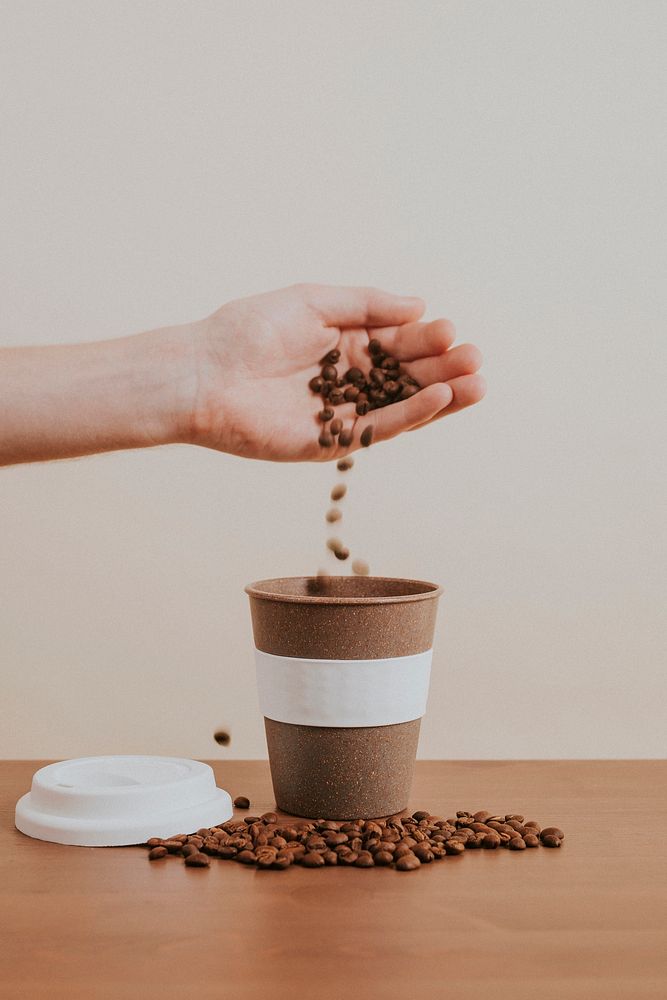 Hand pouring coffee beans into a cork coffee cup