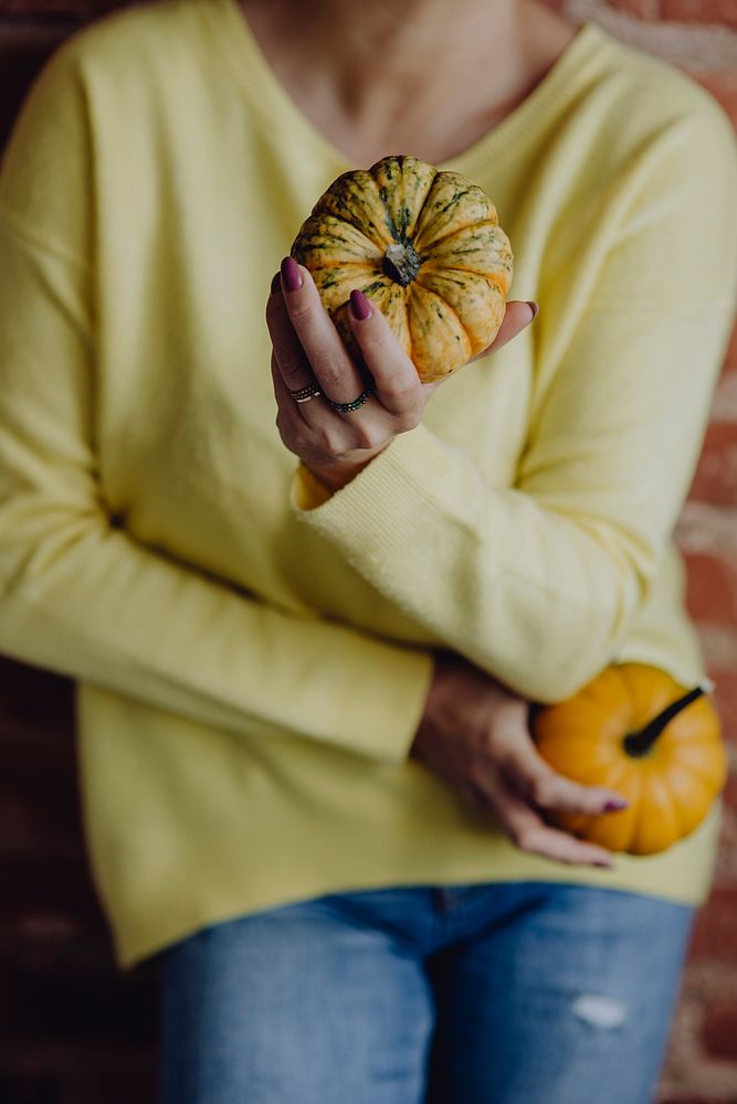 Woman in a yellow sweater holding pumpkins in her hands