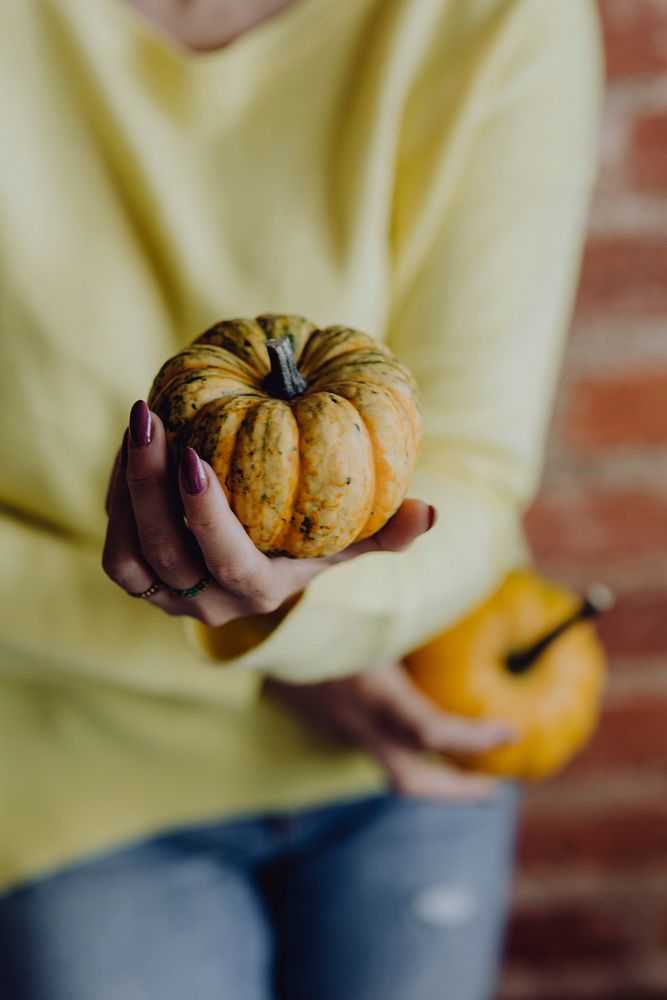 Woman in a yellow sweater holding pumpkins in her hands