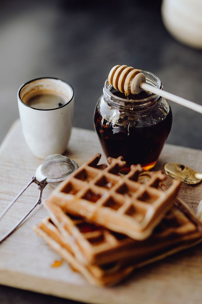 Waffle and slices of banana on a wooden tray next to a honey jar
