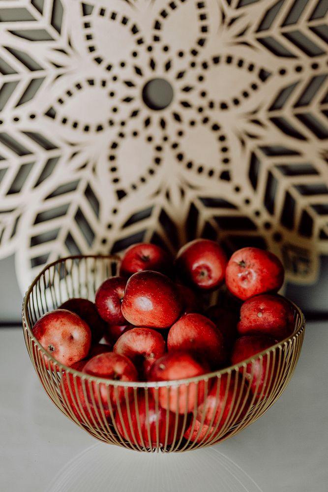 Fresh red apples in a brass basket on a white table