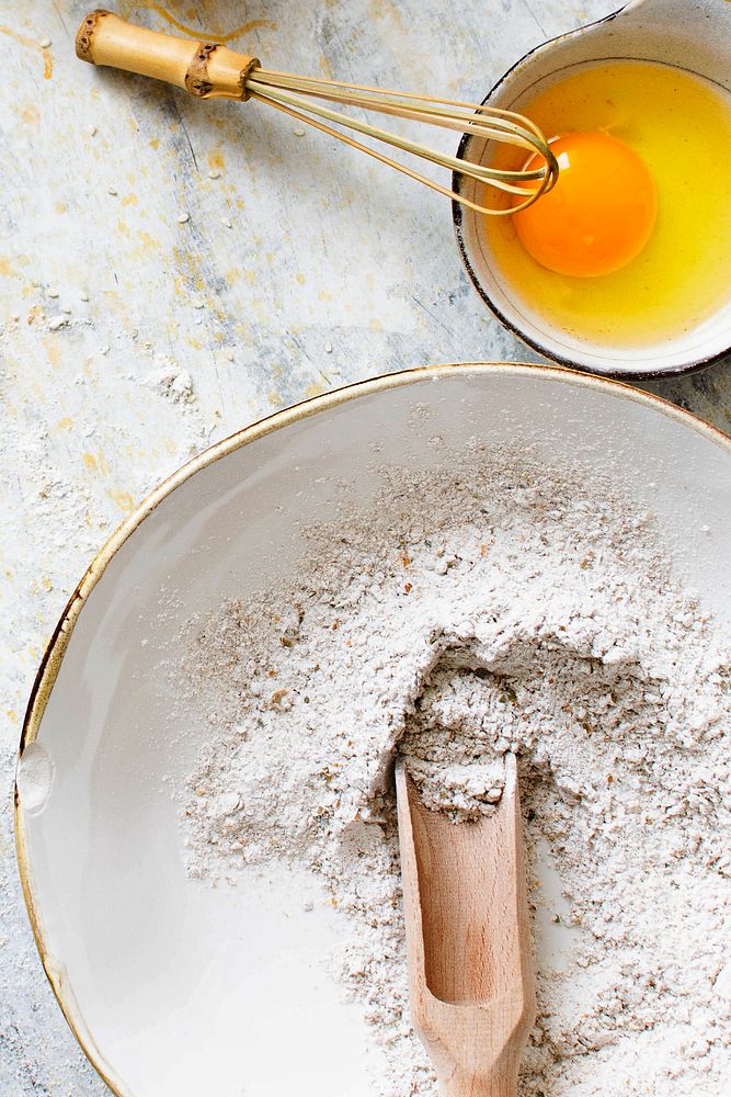 Rye flour with a wooden scoop next to a bowl of fresh egg flatlay