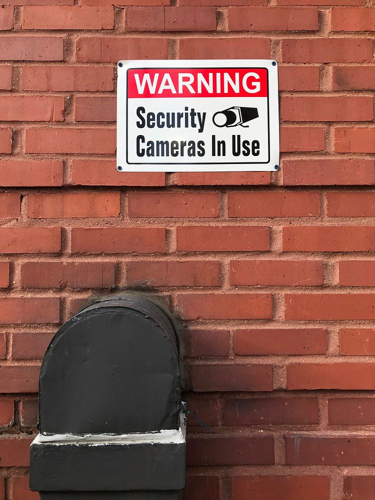 Warning security cameras in use sign on a brick wall