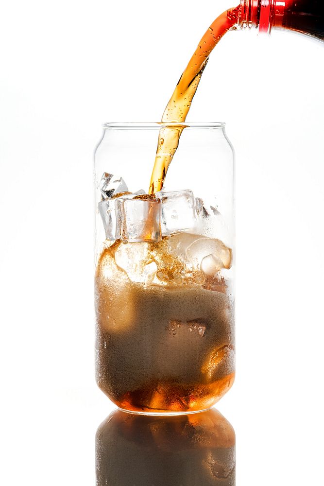 Cold carbonated drink being poured over ice cubes in a can shaped glass 