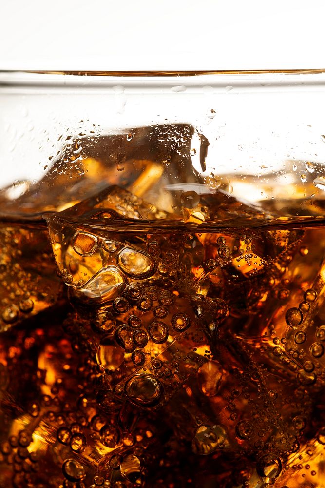 Cold carbonated drink over ice cubes in a glass close up 