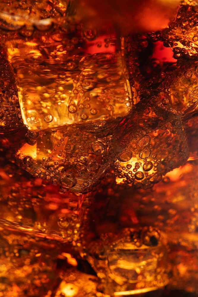 Cold carbonated drink over ice cubes in a glass close up 