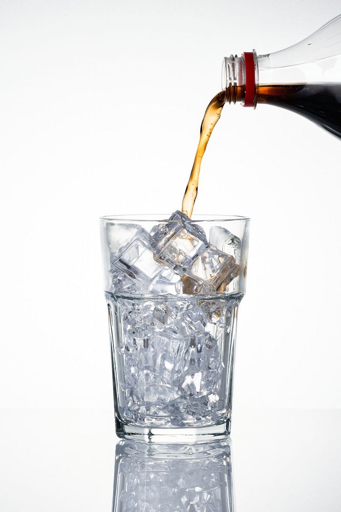 Cold carbonated drink being poured over ice cubes into a glass 