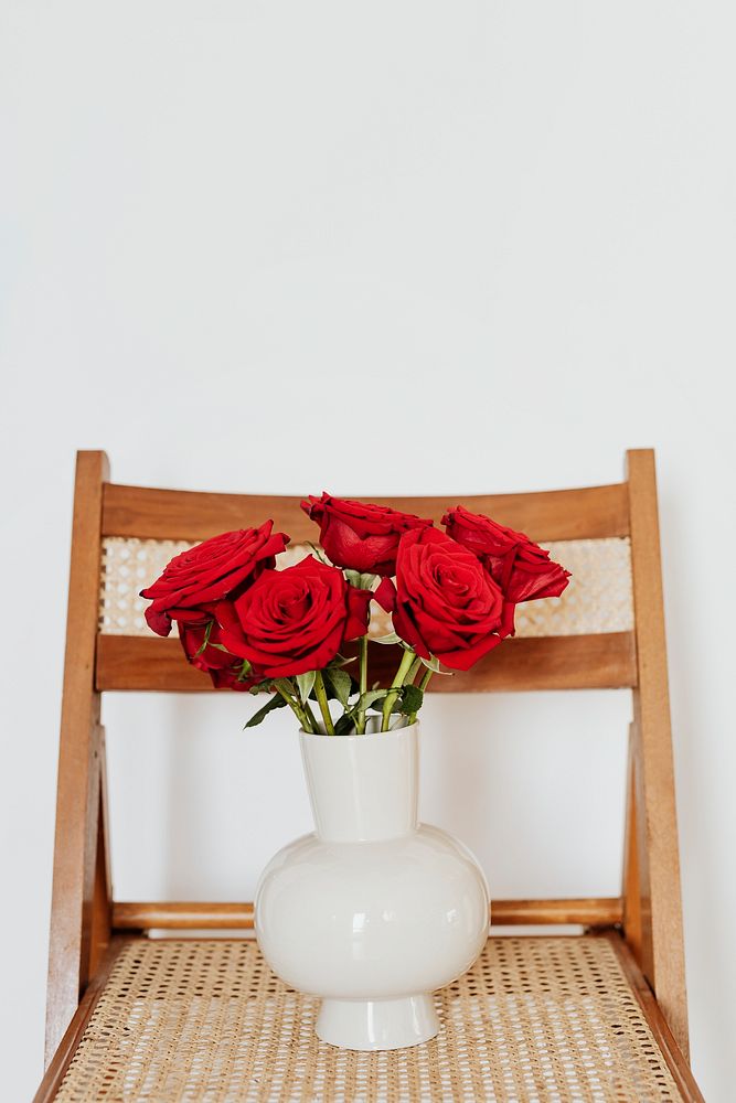 Red roses in a white vase on a wooden chair