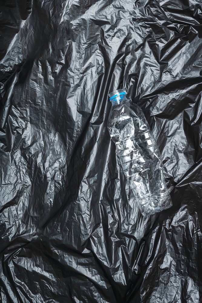 Crumpled plastic bottle on a black disposable trash bag 