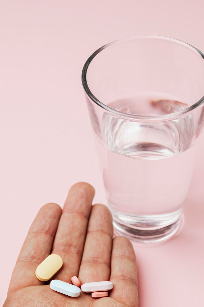 Hand of patient with pills and a glass of water