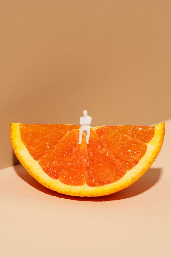 Tiny man sitting on an orange wedge