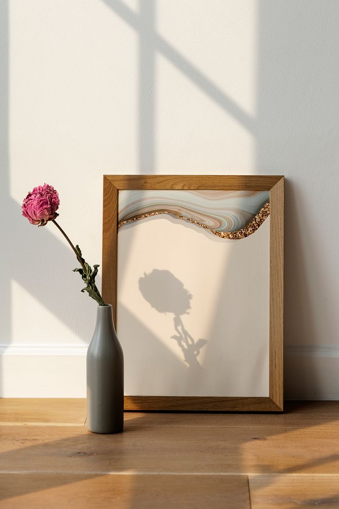 Dried pink peony flower in a gray vase by a wooden frame on the floor