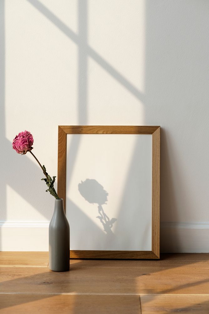Dried pink peony flower in a gray vase by a wooden frame on the floor